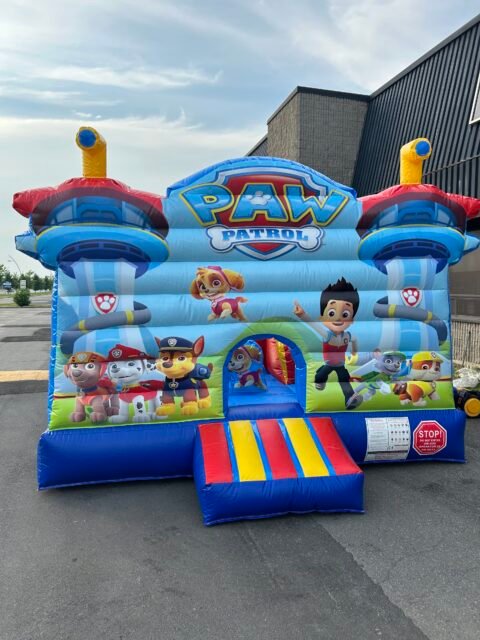 Jeu gonflable Pat&rsquo; Patrouille XL gonfl&eacute; dans un stationnement&nbsp;: deux tourelles de guet &agrave; p&eacute;riscope jaune sur c&ocirc;ne rouge, grand &eacute;cusson PAW PATROL au centre du fronton, personnages de la s&eacute;rie imprim&eacute;s sur la fa&ccedil;ade et marche d'acc&egrave;s ray&eacute;e rouge, jaune et bleu devant l'entr&eacute;e
