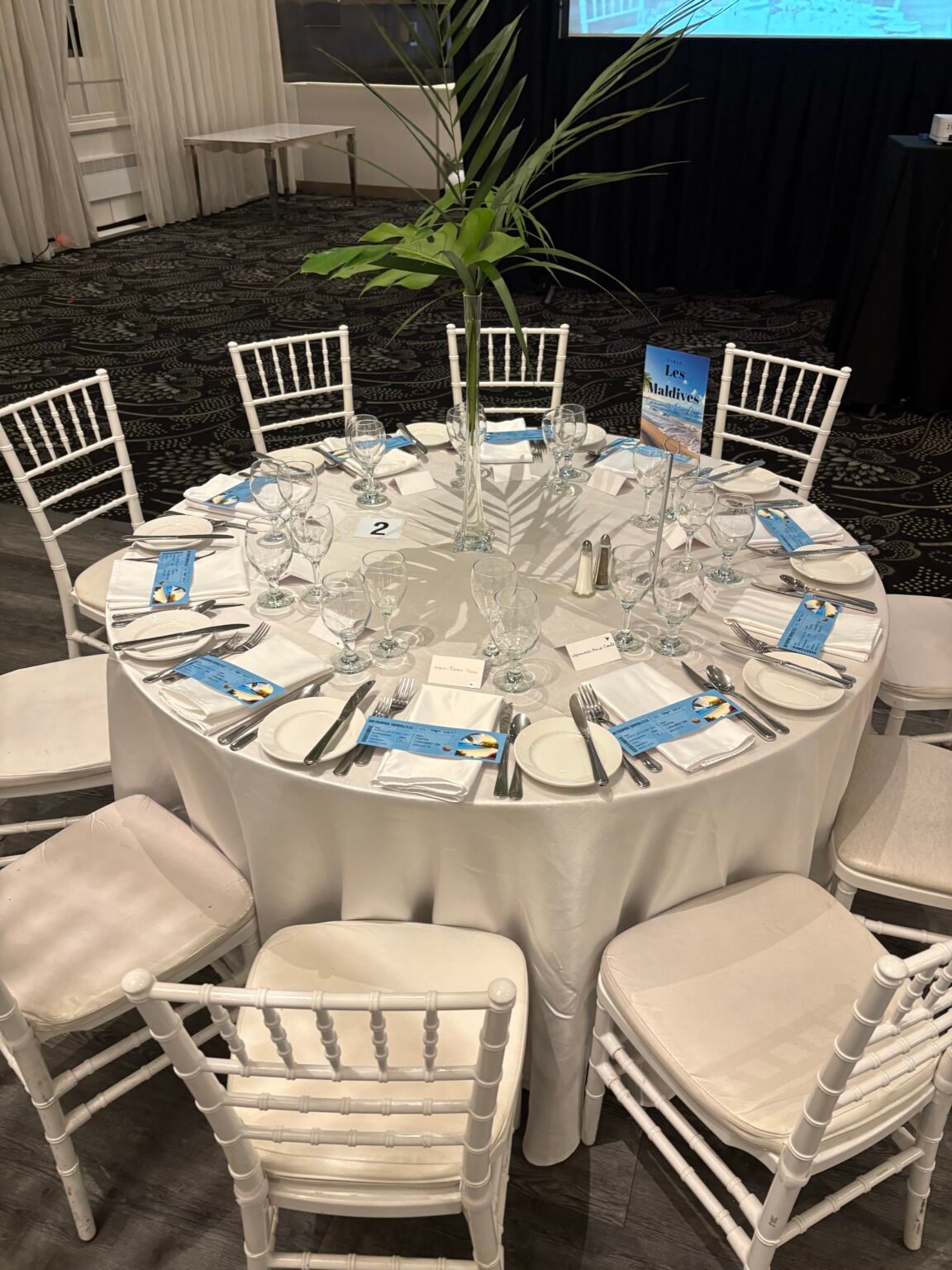 Table ronde dress&eacute;e par &Eacute;venox : nappe blanche satin&eacute;e, chaises Chiavari blanches, assiettes, couverts, verres et serviettes