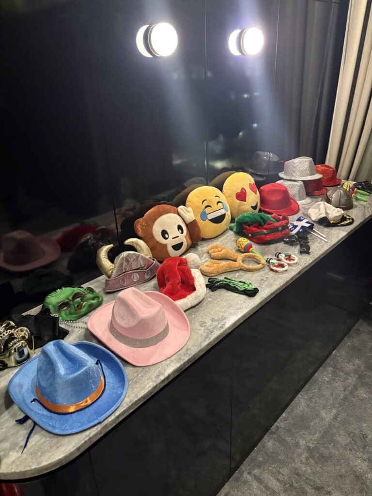 Table d&rsquo;accessoires du photobooth &Eacute;venox sous deux projecteurs : chapeaux, masques, couronnes et peluches &eacute;moji