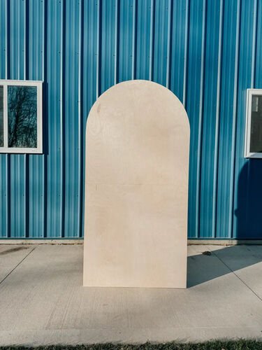 Panneau de contreplaqué brut à sommet arrondi, appuyé contre un mur de tôle bleue à notre entrepôt