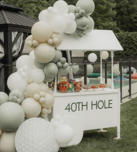 Chariot &agrave; bonbons blanc &agrave; toit, garni de sacs de friandises, install&eacute; dans une cour et entour&eacute; d'une guirlande de ballons verts et cr&egrave;me