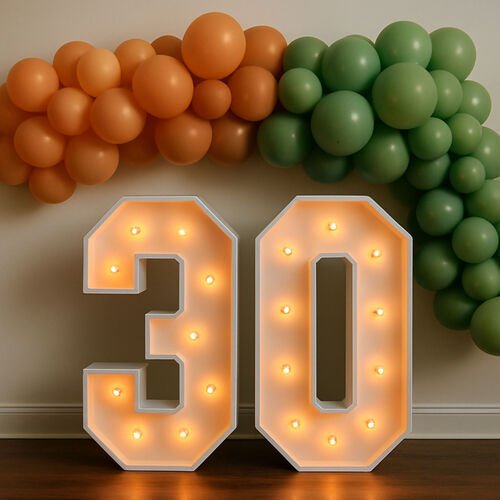 Chiffres lumineux géants formant 30, ampoules allumées, devant une guirlande de ballons orange et verts