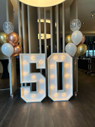 Chiffres lumineux géants formant 50 dans un hall, encadrés de deux bouquets de ballons blancs et dorés
