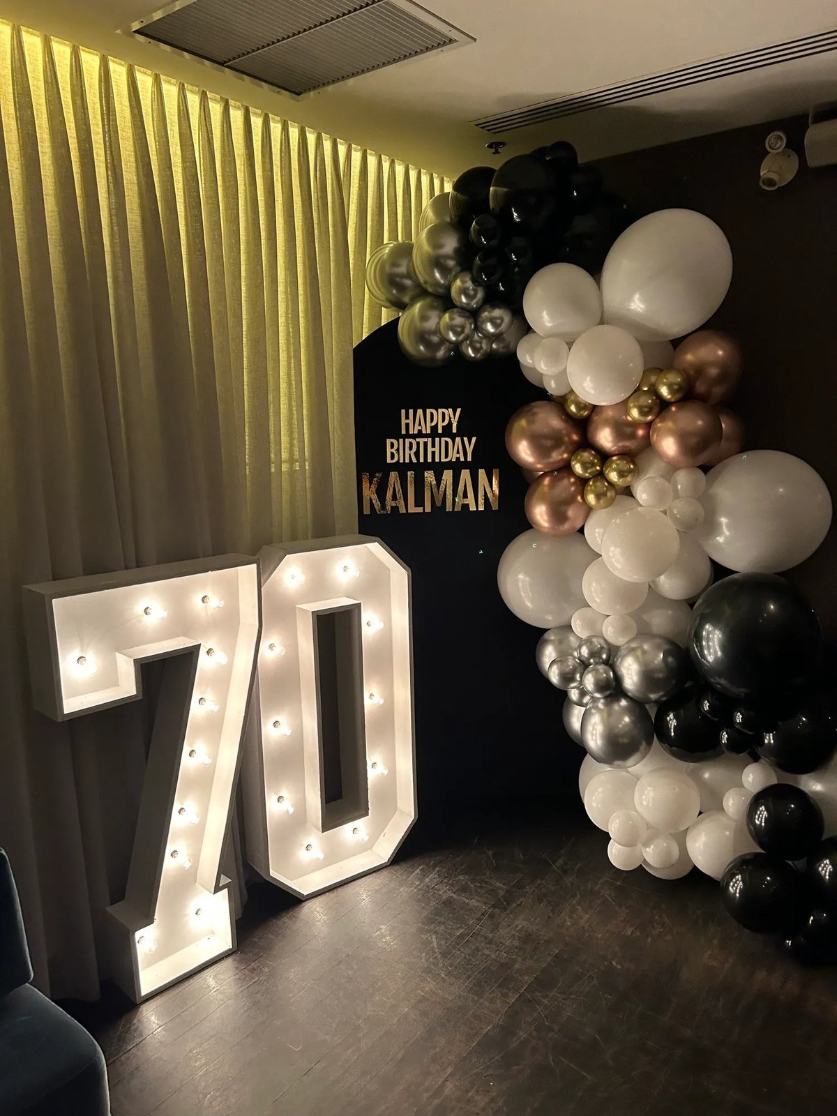 Chiffres lumineux g&eacute;ants formant 70 dans une salle, devant une guirlande de ballons noirs, blancs et cuivr&eacute;s