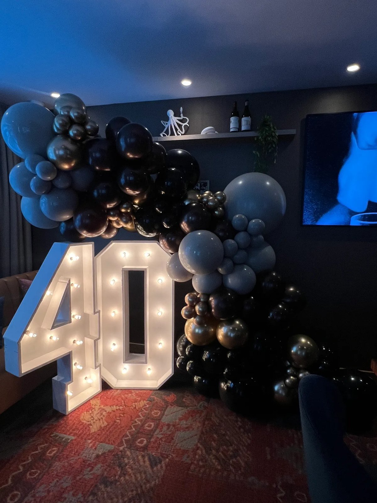 Les chiffres lumineux 4 et 0 dans un salon sombre, envelopp&eacute;s d'une guirlande de ballons noirs, bleus et dor&eacute;s