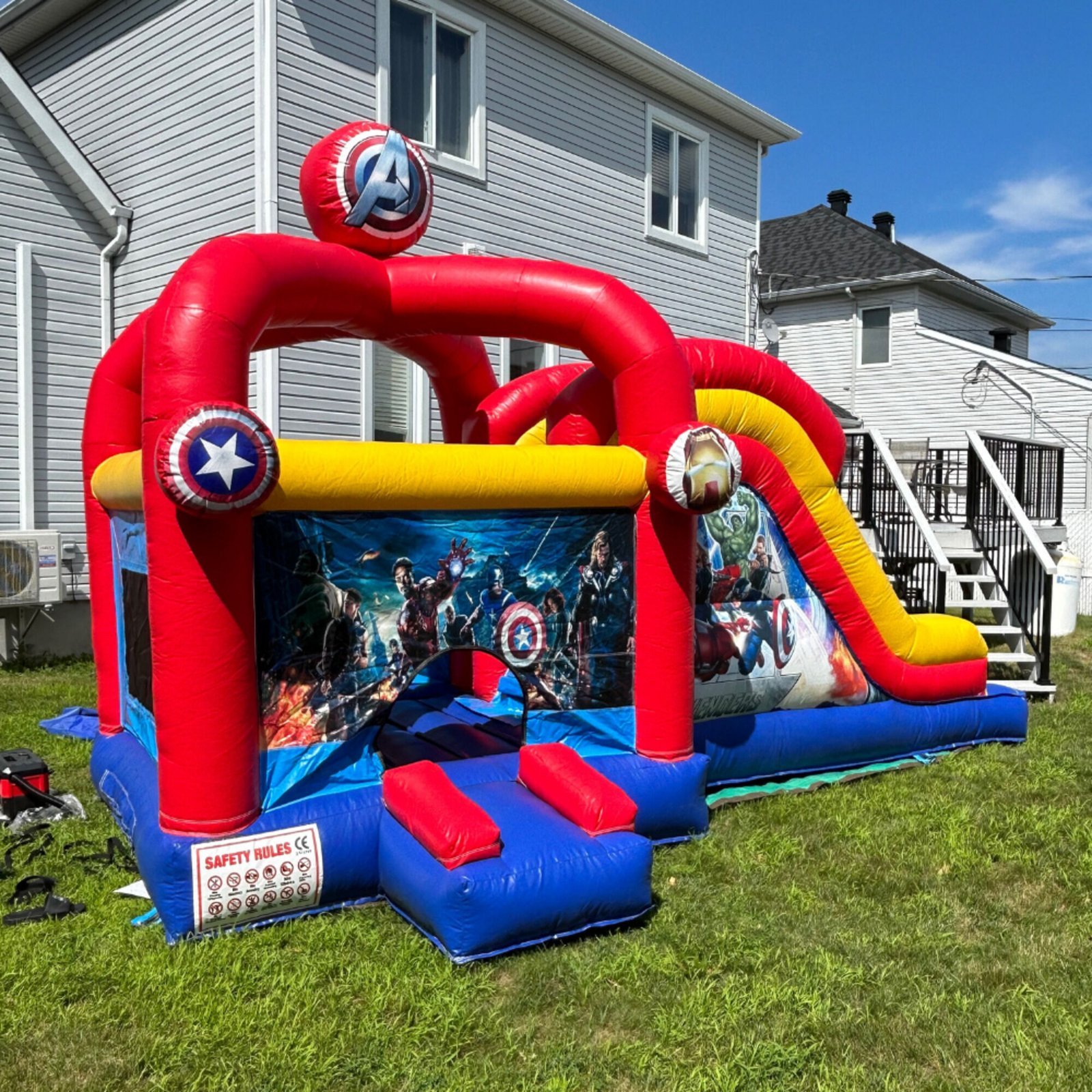 Jeu gonflable rouge, bleu et jaune aux couleurs des Avengers, avec glissade sur le côté, monté sur la pelouse d'une cour résidentielle