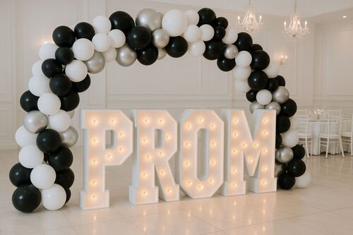 Les lettres lumineuses P R O M sous une arche de ballons noirs, blancs et argent&eacute;s, dans une salle &agrave; lustres
