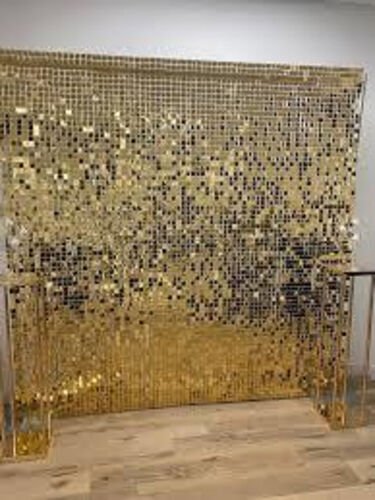 Mur de paillettes carrees dorees monte sur un cadre autoportant, dans une piece a plancher de bois