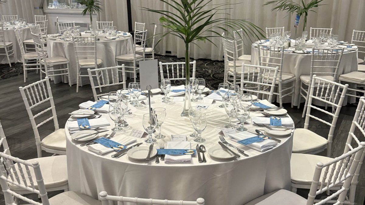 Table ronde nappée de blanc dans une salle de réception, entourée de chaises Chiavari blanches